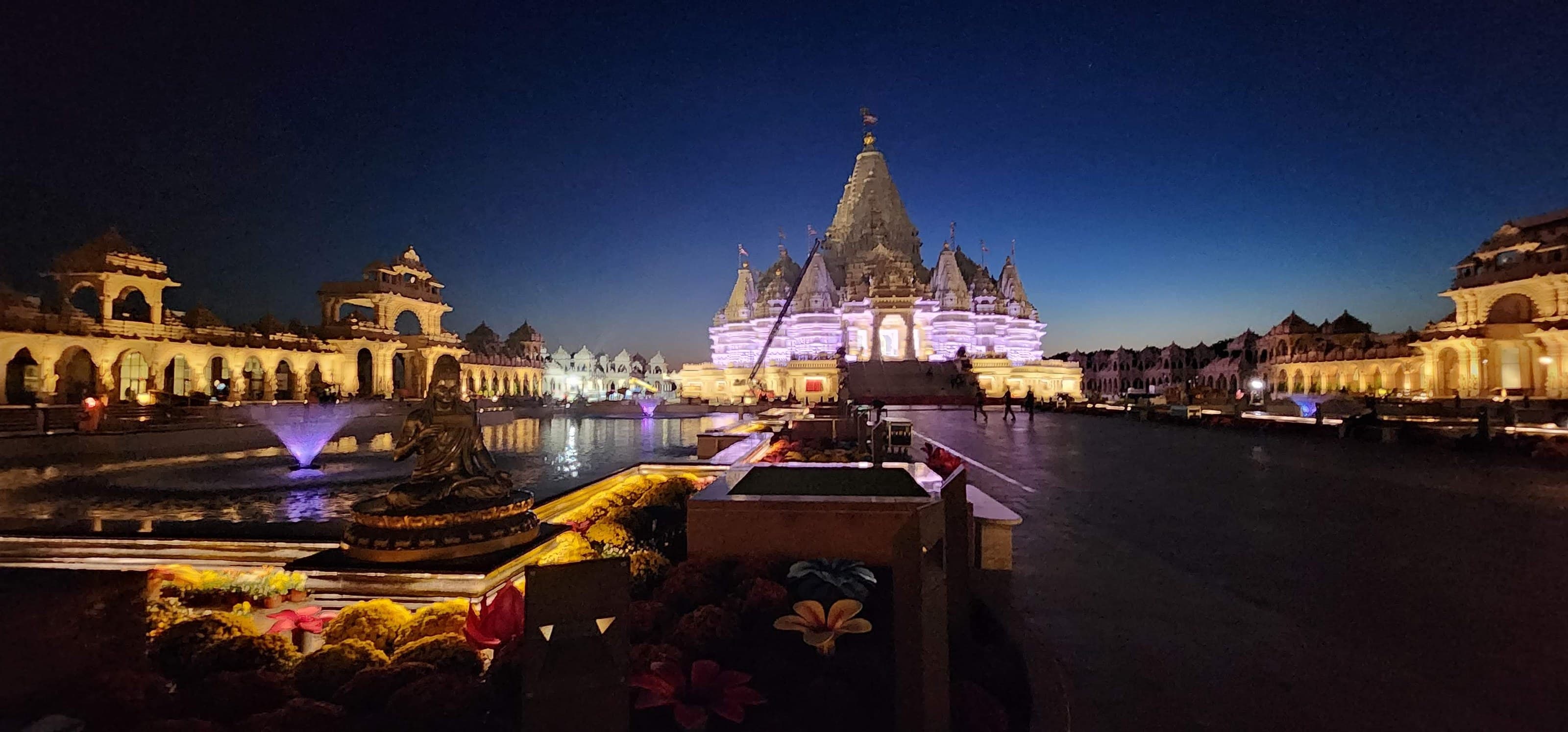 BAPS Swaminarayan Akshardham lit at night beside its reflecting pool, fountains, flower beds, and grounds in Robbinsville.