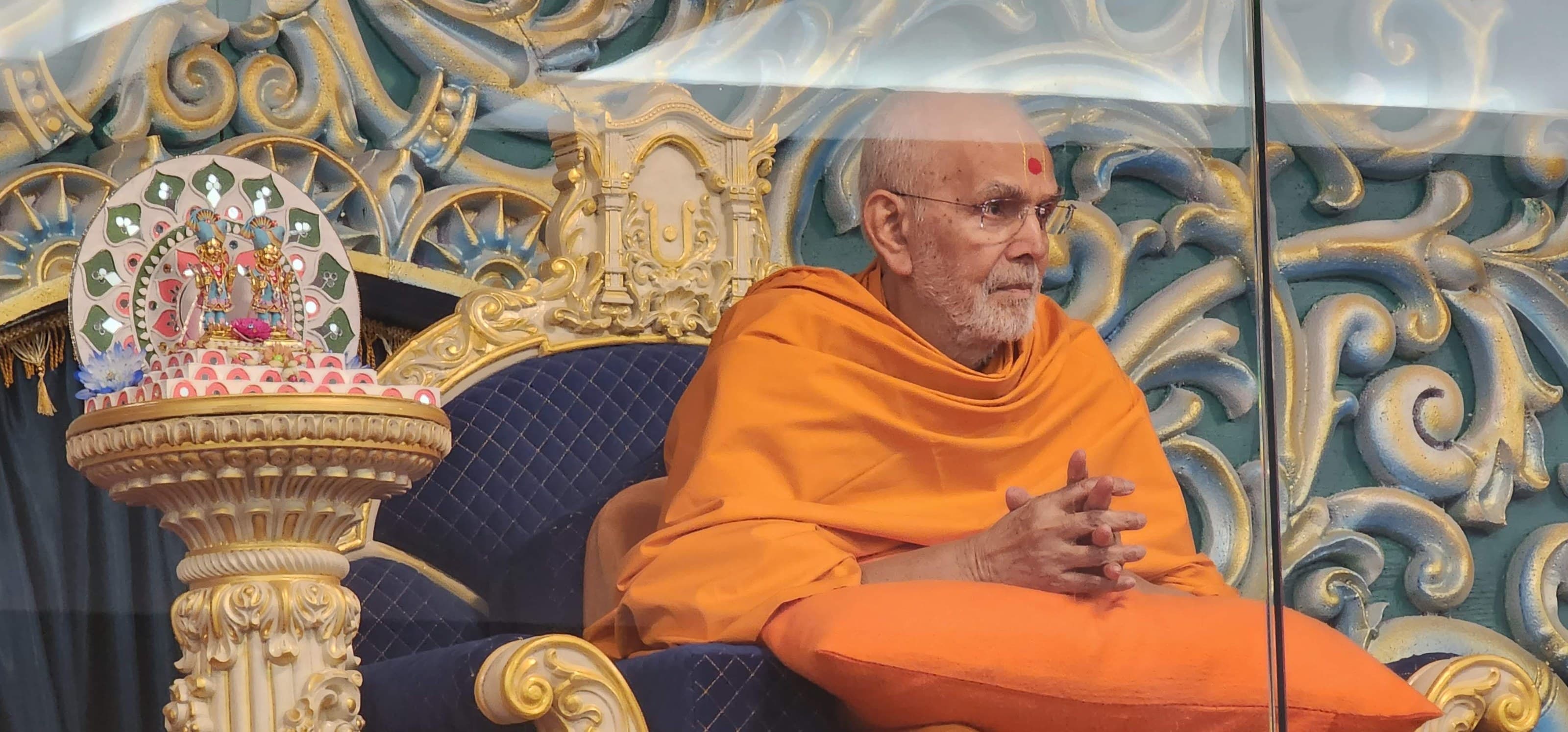 Mahant Swami Maharaj seated beside the murti of Akshar-Purushottam Maharaj.
